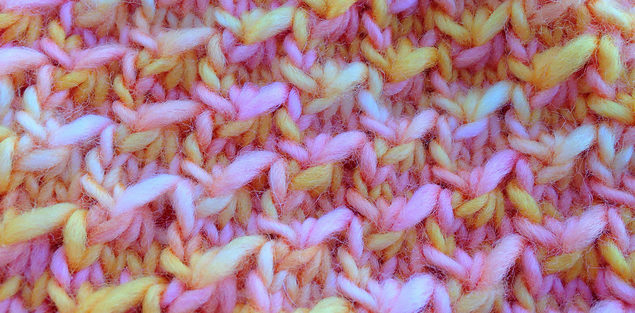 Close up of knitted fabric in Danu, 100% merino single ply yarn.  Colors are pink, white, and tangerine.
